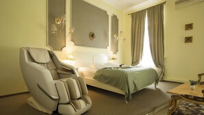 Ein Hotelzimmer mit Massagesessel, einem Bett mit grüner Bettdecke, einem Nachttisch mit Lampe und einem kleinen Tisch mit einer Vase.