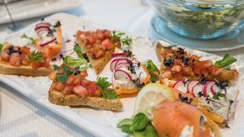 A white rectangular plate with various appetizers, including smoked salmon, tomatoes, and herbs.