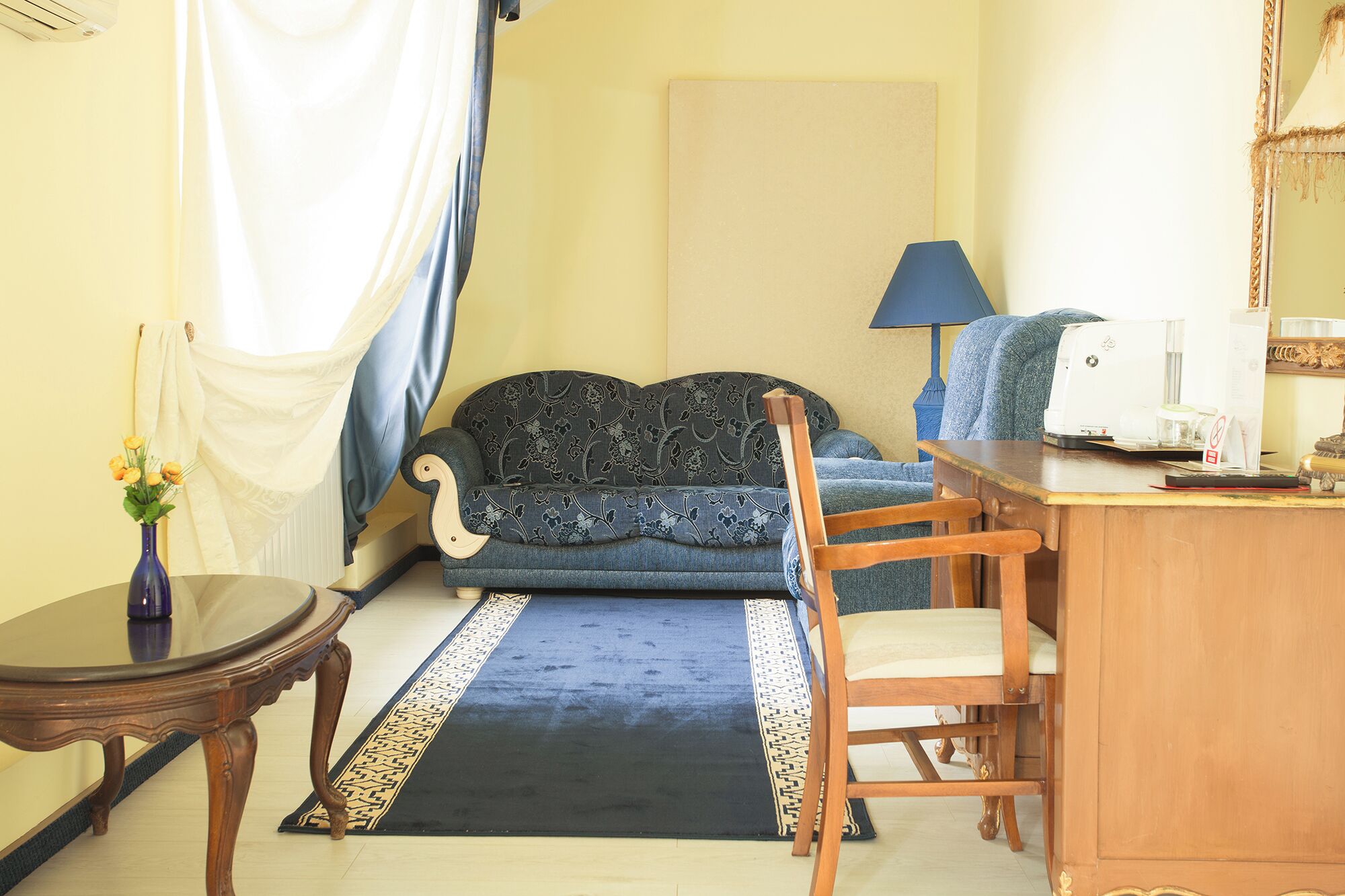 Una habitación con un sofá, una silla de madera, una mesita, una máquina de coser y un jarrón con flores.