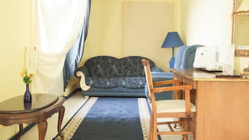 Una habitación con un sofá, una silla de madera, una mesita, una máquina de coser y un jarrón con flores.