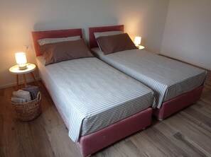 Een tweepersoonsbed met streepjesbeddengoed, twee kussens, een bedlampje en een geweven mand met handdoeken.
