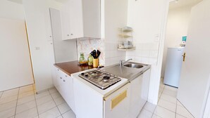 Una cucina compatta con mobili bianchi, un piano cottura a gas, un lavello e un piccolo frigorifero.