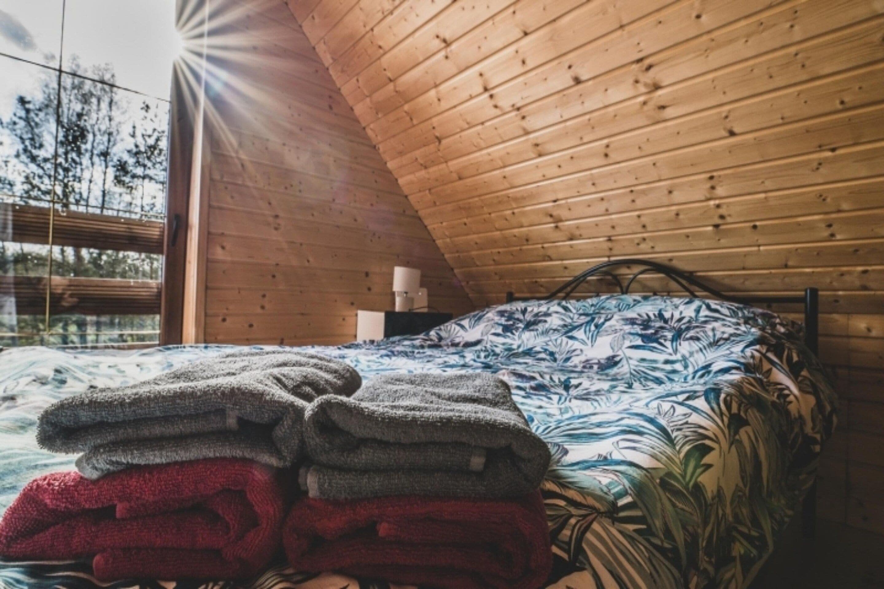 A bedroom with a wooden ceiling, a bed with a floral bedspread, and a window with a view of trees.