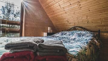 A bedroom with a wooden ceiling, a bed with a floral bedspread, and a window with a view of trees.