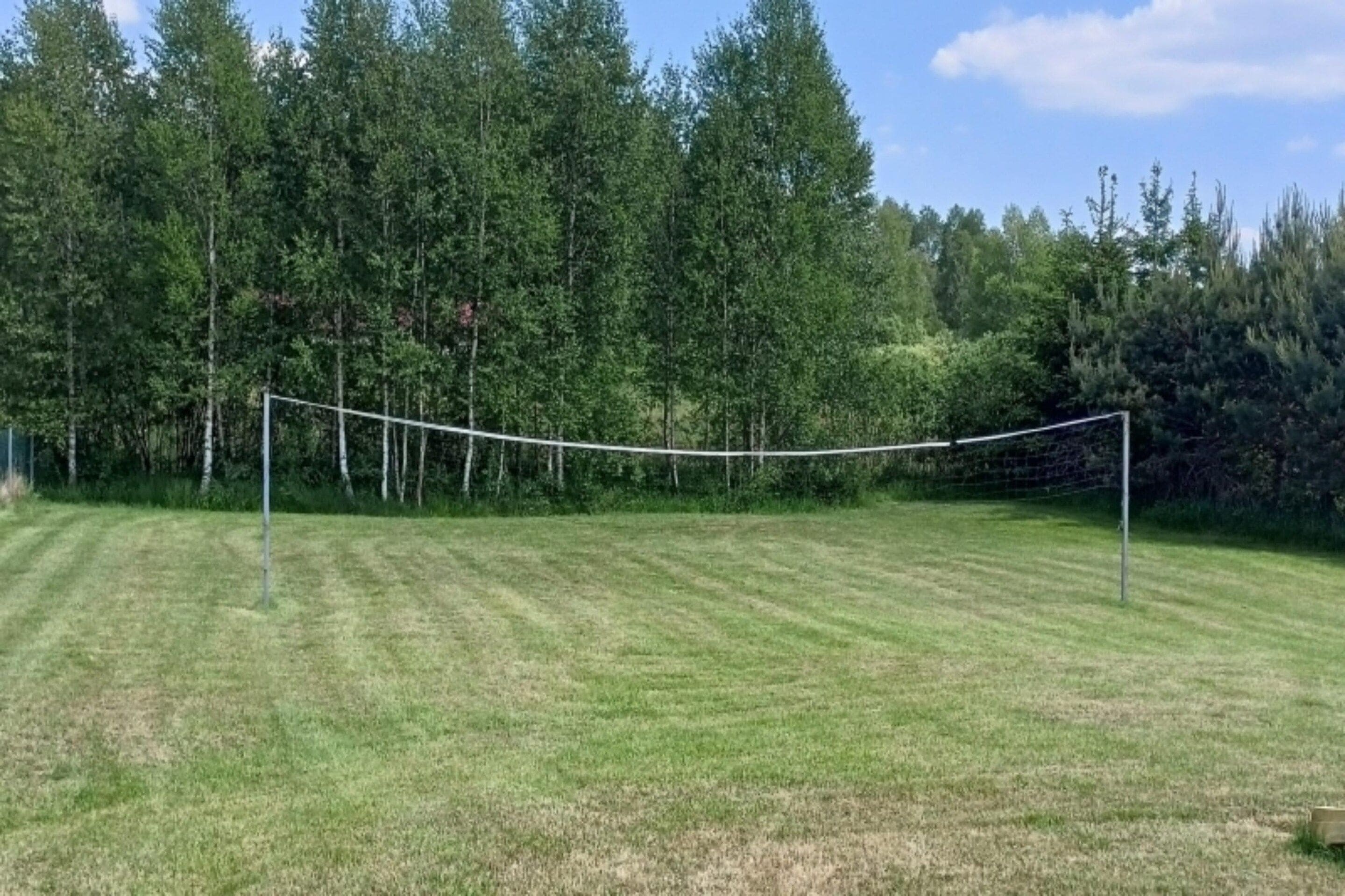 A volleyball net in a grassy field with trees in the background.