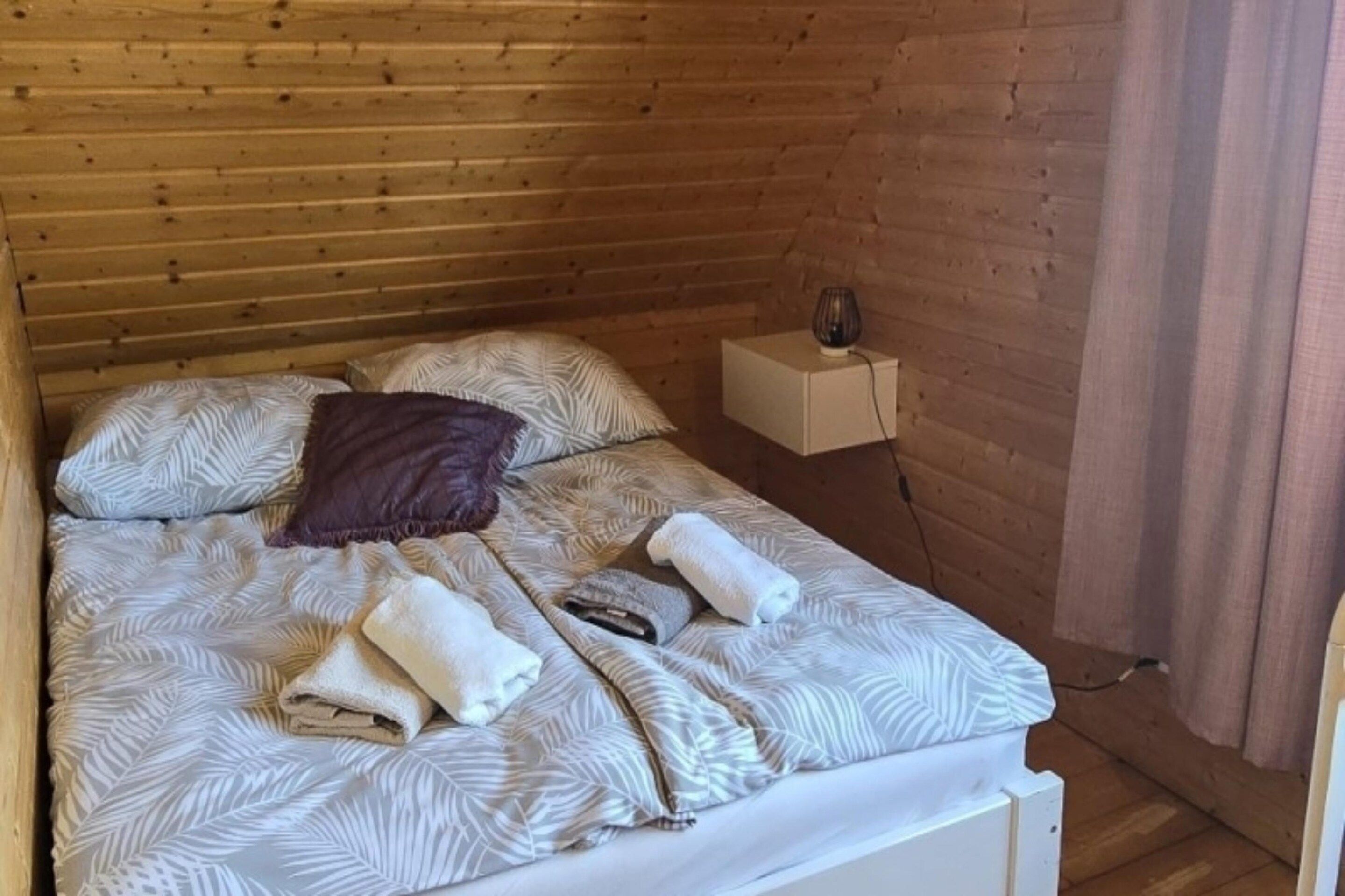 A bed with patterned bedding, a pillow, and rolled towels.