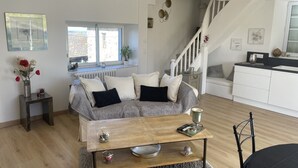 Ein modernes Wohnzimmer mit grauem Sofa, Couchtisch aus Holz und einer Treppe, die zur Küche führt.