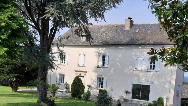 Ein zweistöckiges Haus mit gepflegtem Rasen, einem großen Baum und einer Schotterauffahrt.