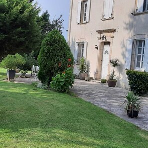A building with a paved entrance, a well-maintained lawn, and various potted plants. - COUNTRY GITE (Morlhon-le-Haut)