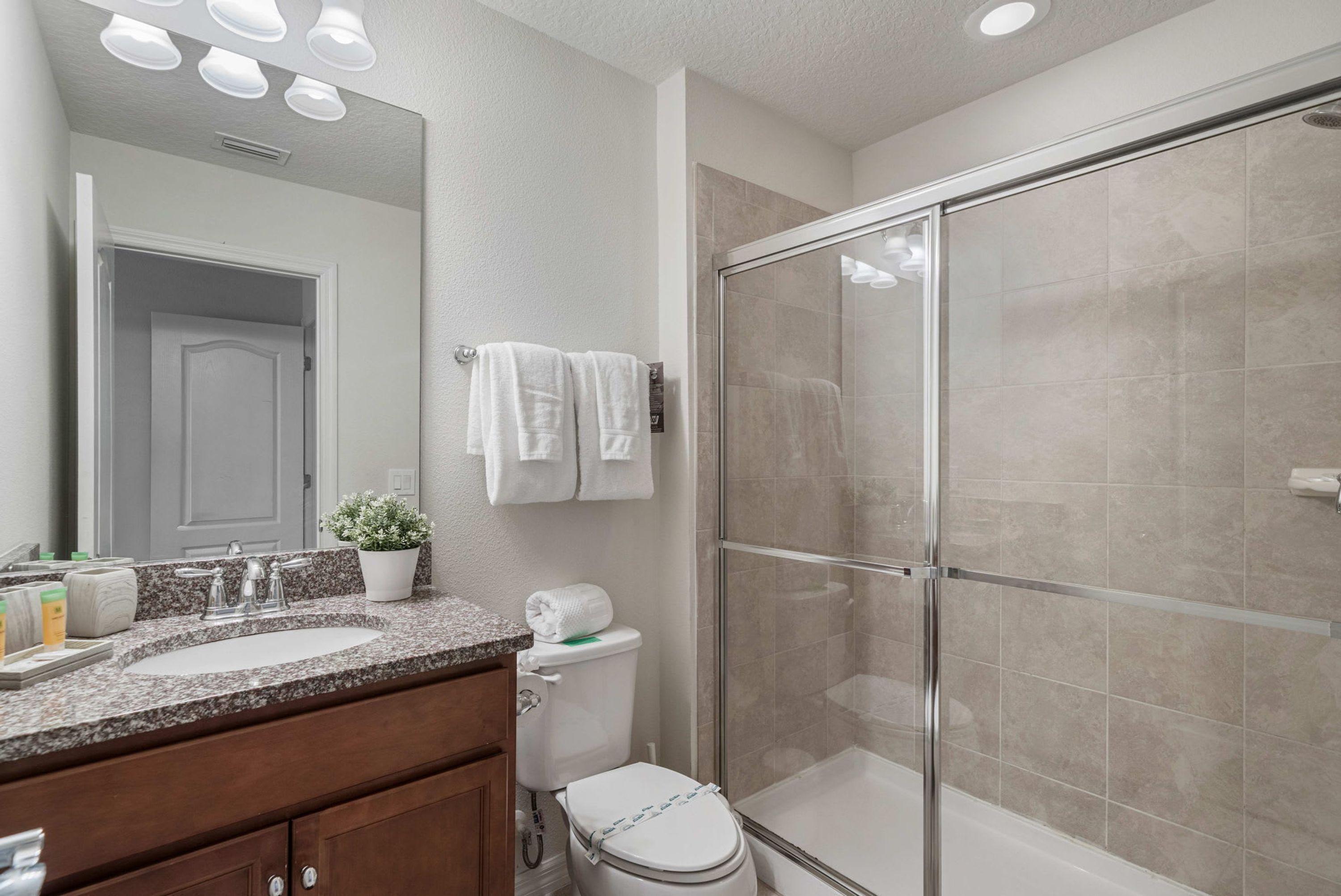 A bathroom with a double sink, a toilet, a shower with glass doors, and a mirror above the sink.