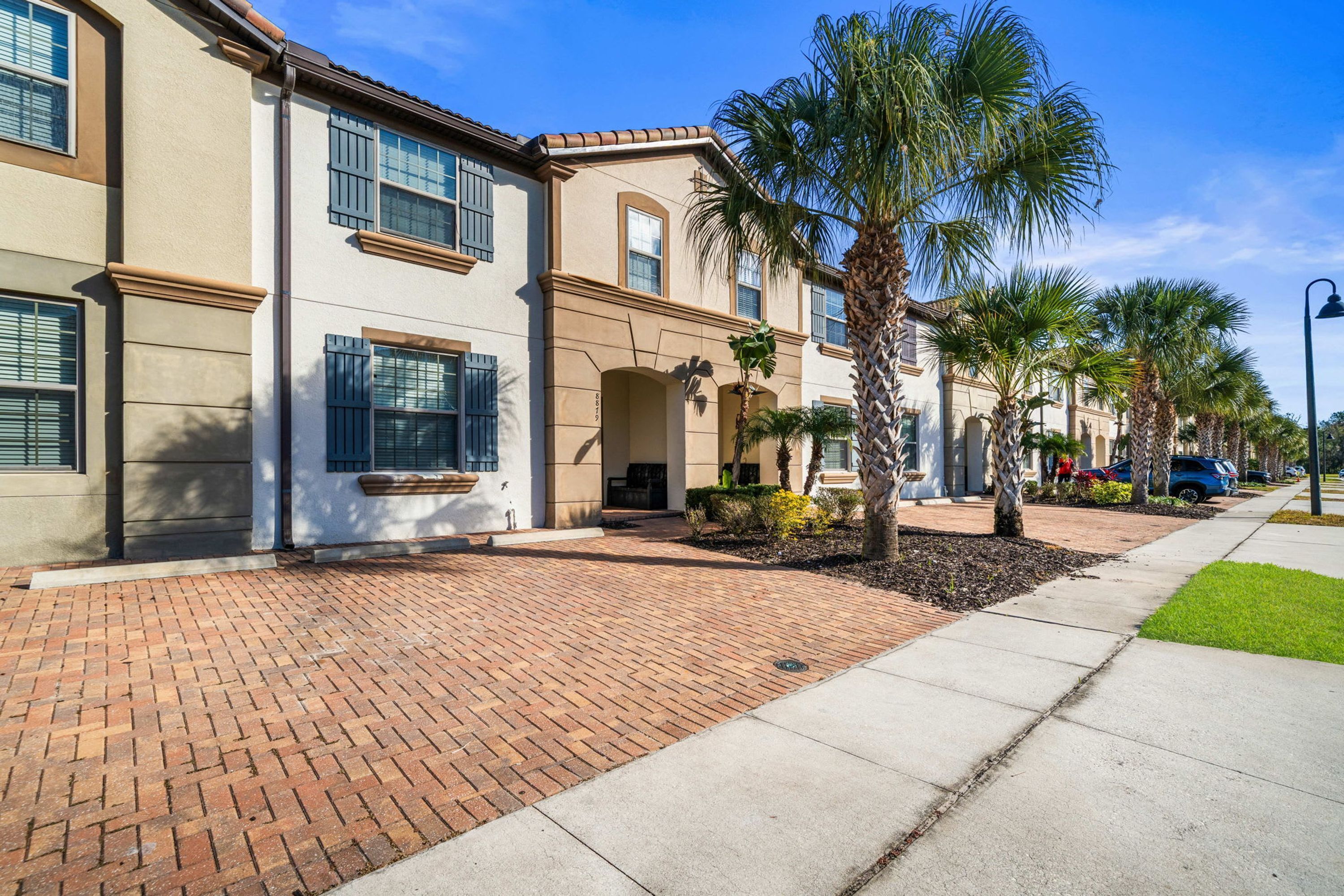 A row of townhouses with brick walkways and palm trees.
