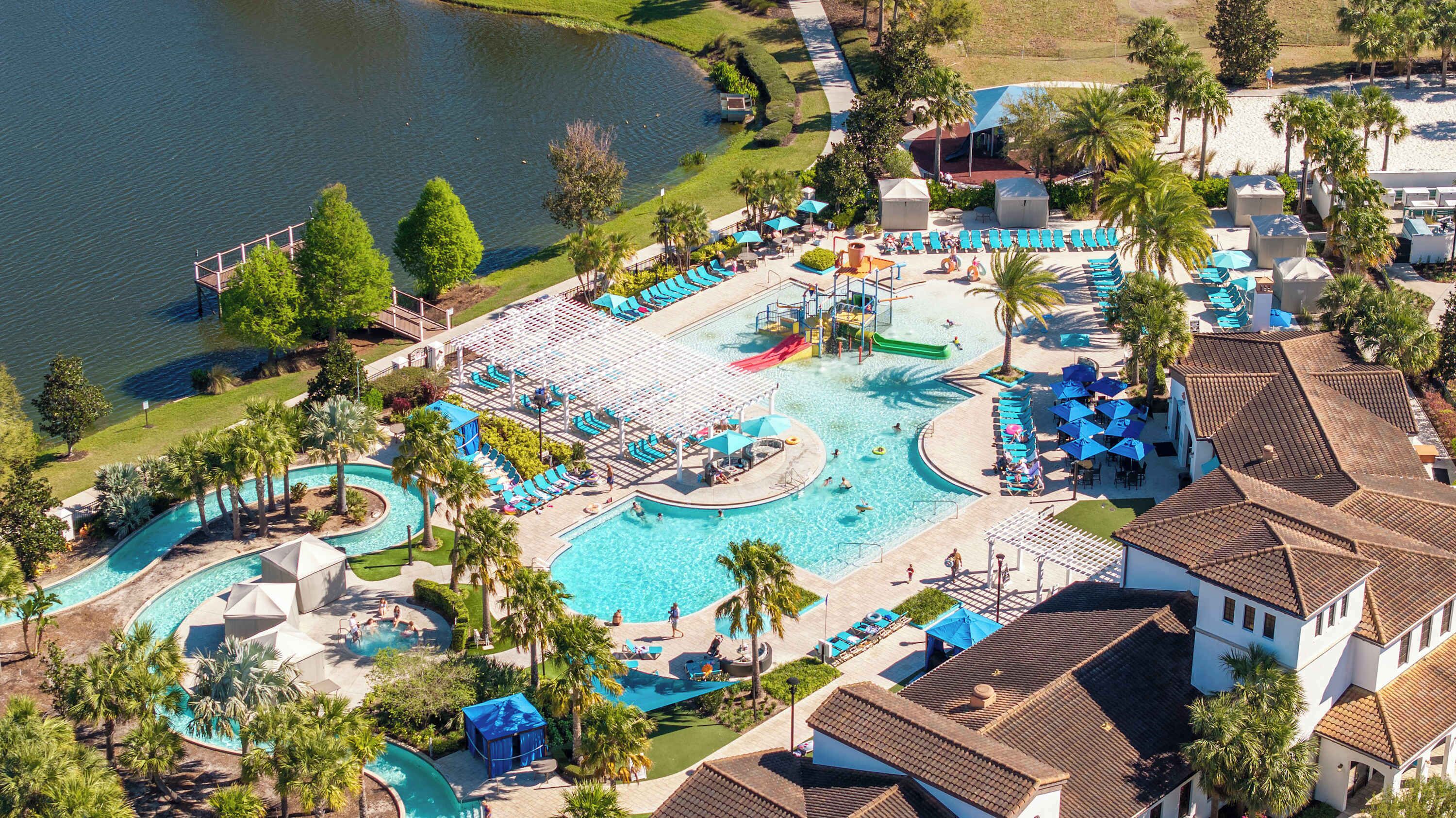 An aerial view of a resort with a large central pool, multiple smaller pools, and a water slide.