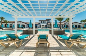Ein Poolbereich mit Liegestühlen und Sonnenschirmen, eine überdachte Pergola und ein Gebäude im Hintergrund.