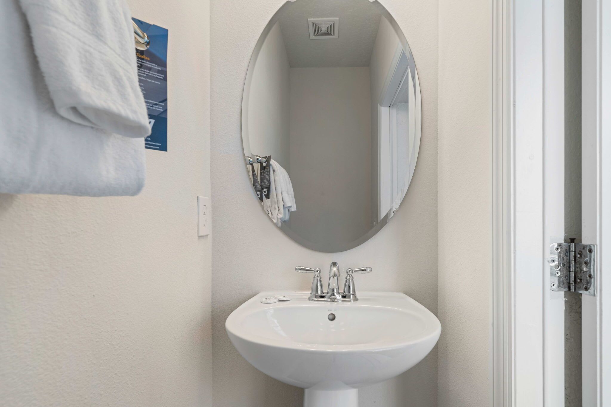 Une salle de bain avec un lavabo blanc, un miroir rond et une serviette accrochée au mur.