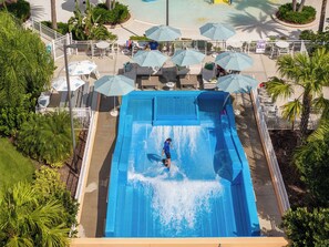 Eine Rutsche in einem Resort mit Liegestühlen und Sonnenschirmen rund um einen Pool.