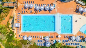 Eine Vogelperspektive auf ein Resort mit zwei Schwimmbecken, Liegestühlen und Sonnenschirmen.