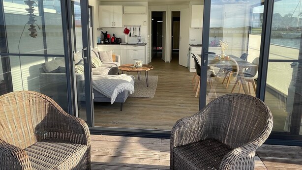 Ein moderner Wohnraum mit Balkon, Rattanmöbeln, einer Küche und einem Essbereich.