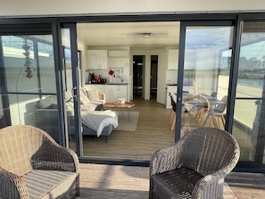 A modern living space with a balcony, wicker furniture, a kitchen, and a dining area. - Hausboot Charlotte im Hafen in Ribnitz-damgarten (Ribnitz-Damgarten)