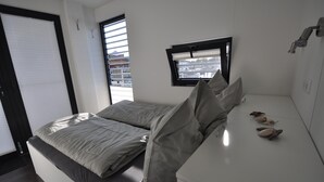 Ein modernes Schlafzimmer mit einem Bett, einem kleinen Fenster und einem Nachttisch mit dekorativen Muscheln.