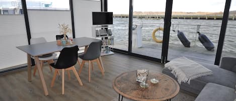 A modern interior with a dining area, sofa, and a view of the water.