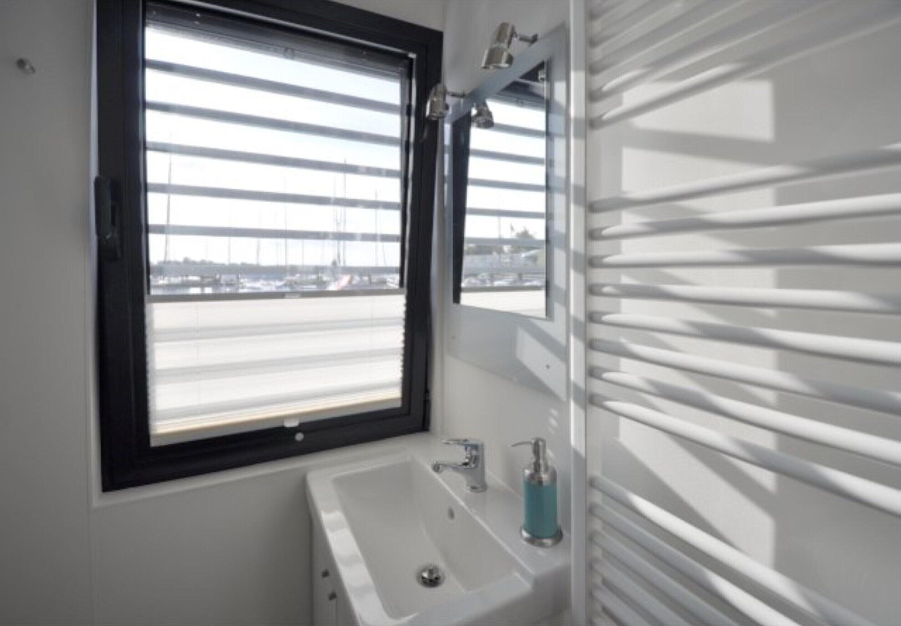 Une salle de bain avec une fenêtre, un lavabo et un miroir.