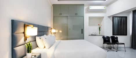 A modern hotel room with a large bed, bedside tables, a desk, a wardrobe, and a seating area with chairs.