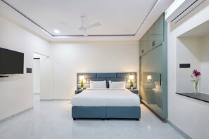 A modern hotel room with a large bed, bedside lamps, a flat-screen TV, and a ceiling fan.