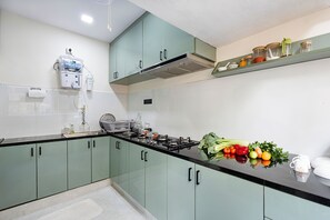 A kitchen with green cabinets, a gas stove, and a variety of fresh produce on the counter.