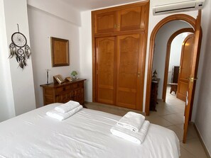 A bedroom with a bed, wooden wardrobe, a desk with a lamp, a dreamcatcher, and a mirror. - Penthouse in Nerja Near Balcon de Europa (Nerja)