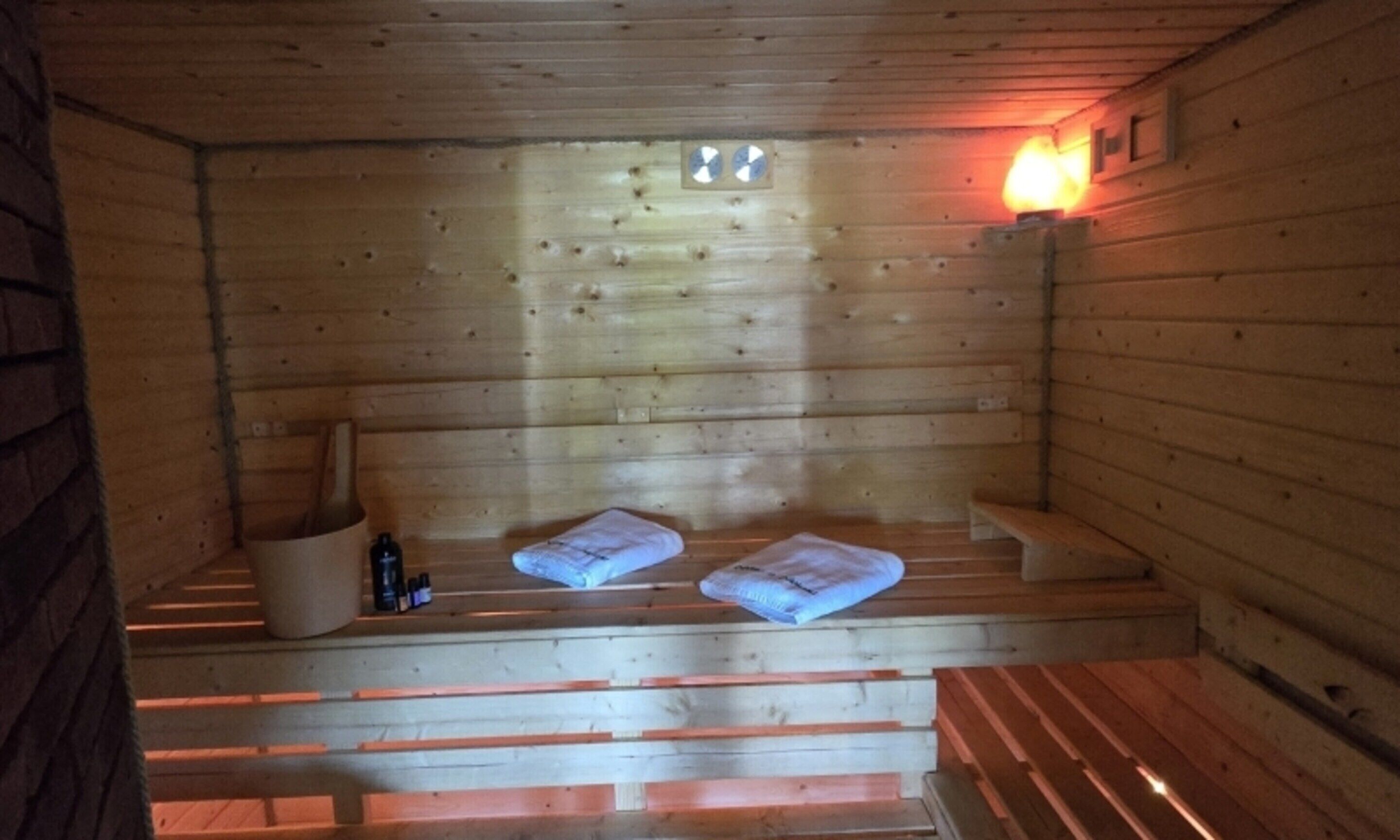 Una sauna de madera con bancos y un asiento, suelo de madera y un aplique en la pared.