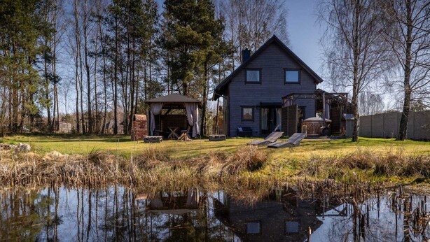 Un chalet rustique avec un étang devant, entouré d’arbres.