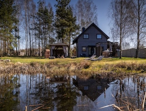 Un chalet rustique avec un étang devant, entouré d’arbres.