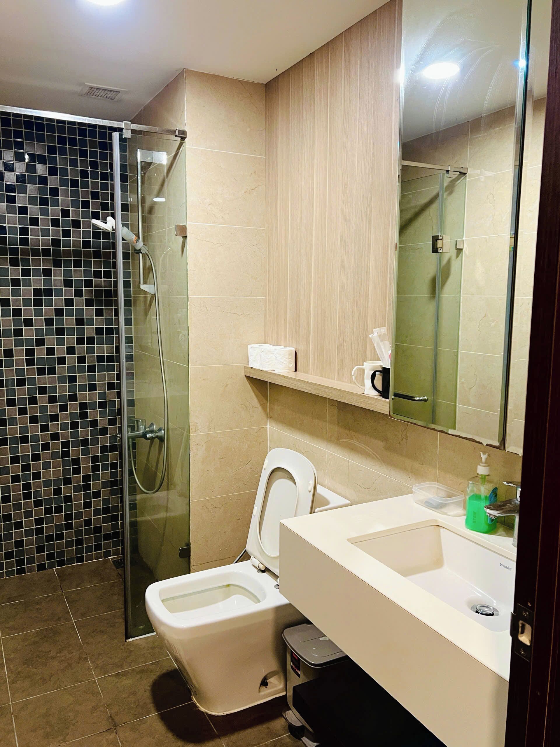 Un baño con ducha de mampara, inodoro y lavabo con espejo arriba.