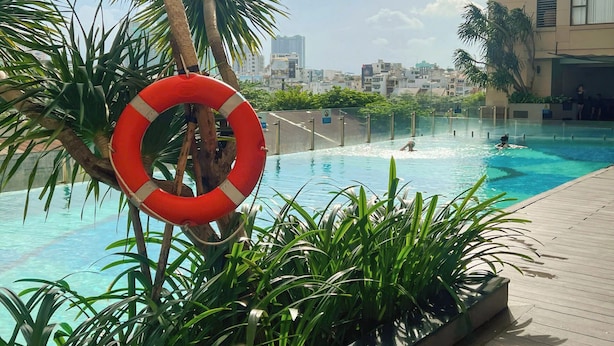 An outdoor swimming pool with a lifebuoy, surrounded by greenery and a cityscape in the background. - THE TRESOR (Ho Chi Minh City)
