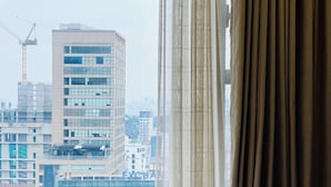 A hotel room with a bed, a window with curtains, and a view of a cityscape with buildings and a crane. - THE TRESOR (Ho Chi Minh City)