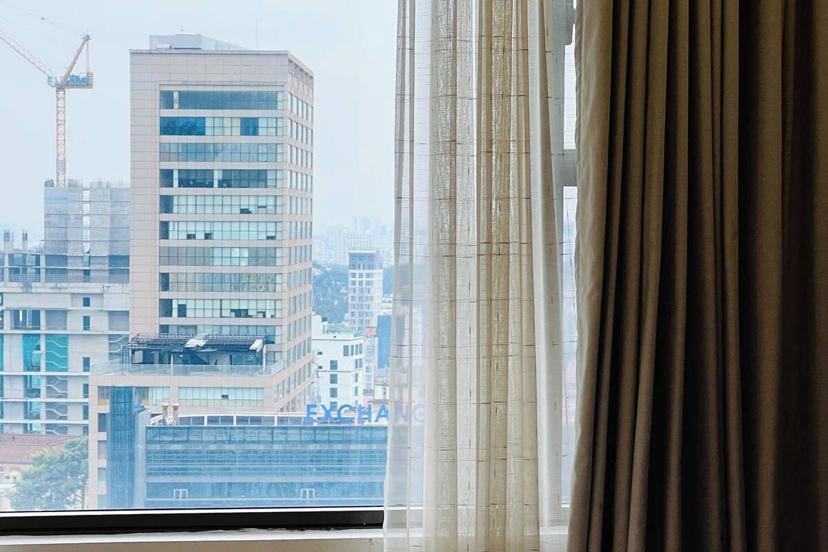 Una camera d'albergo con un letto, una finestra con tende e vista su un panorama urbano con edifici e una gru.