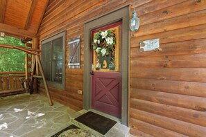 Une cabane en bois avec une porte rouge, un porche en pierre et une balustrade en bois.