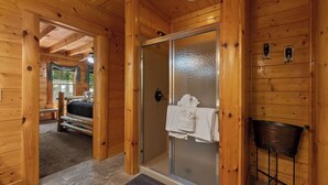 A wooden cabin interior with a glass door leading to a shower area, a bed, and a bench. - Tennessee Treasure: The Smokies' Best-Kept Secret (Sevierville)