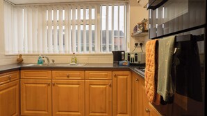 A kitchen with wooden cabinets, a sink, a kettle, and a stove. - No 48 - 3 Bedroom Heworth in York (York)