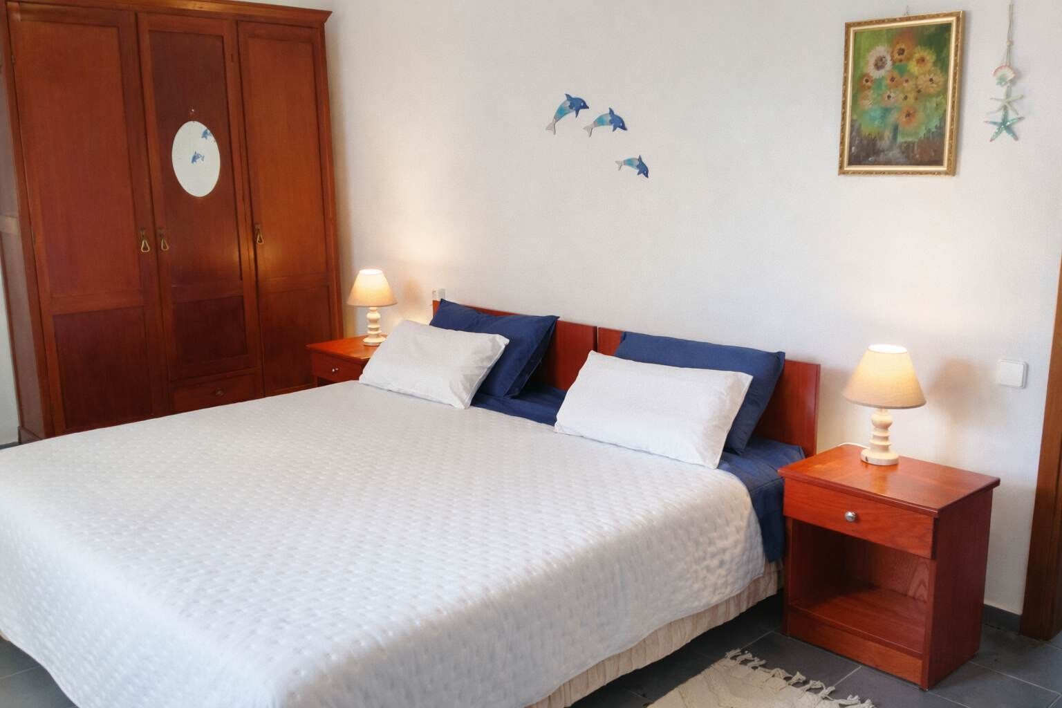 A bedroom with a bed, two bedside tables, a wooden wardrobe, and wall decorations.