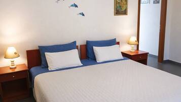 A neatly made bed with blue and white bedding, two bedside tables with lamps, and wall art including a painting and a framed picture.