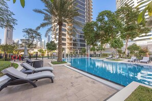 A swimming pool with lounge chairs, surrounded by palm trees and a high-rise building in the background. - A Free Housekeeping Visit FOR Every Stay Between THE 16th FEB AND THE 16th MAR - Stayshort - 1 Bed in Downtown Dubai That Sleeps 4 With Balcony (Dubai)