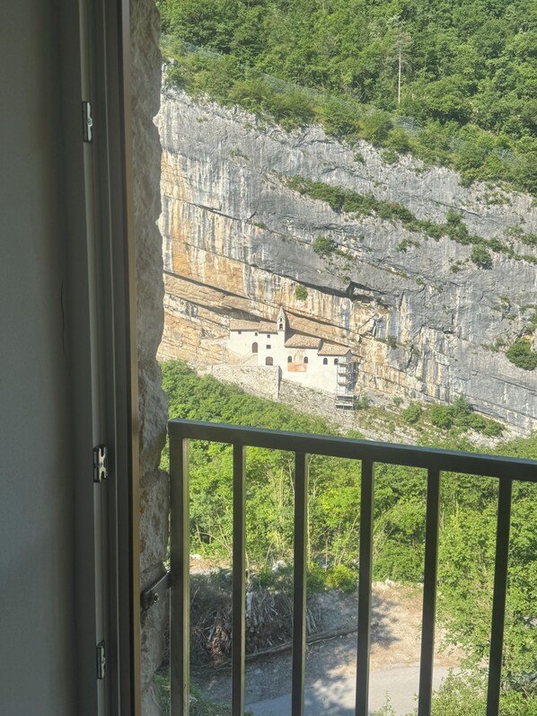 A balcony with a view of a mountainous landscape, a building with a bell tower, and a rocky cliff.