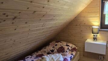 A small, sloped ceiling room with wooden walls, a single bed with floral bedding, and a bedside lamp.