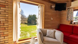 Une pièce avec une grande fenêtre, un canapé rouge, un fauteuil beige et un téléviseur fixé au mur.