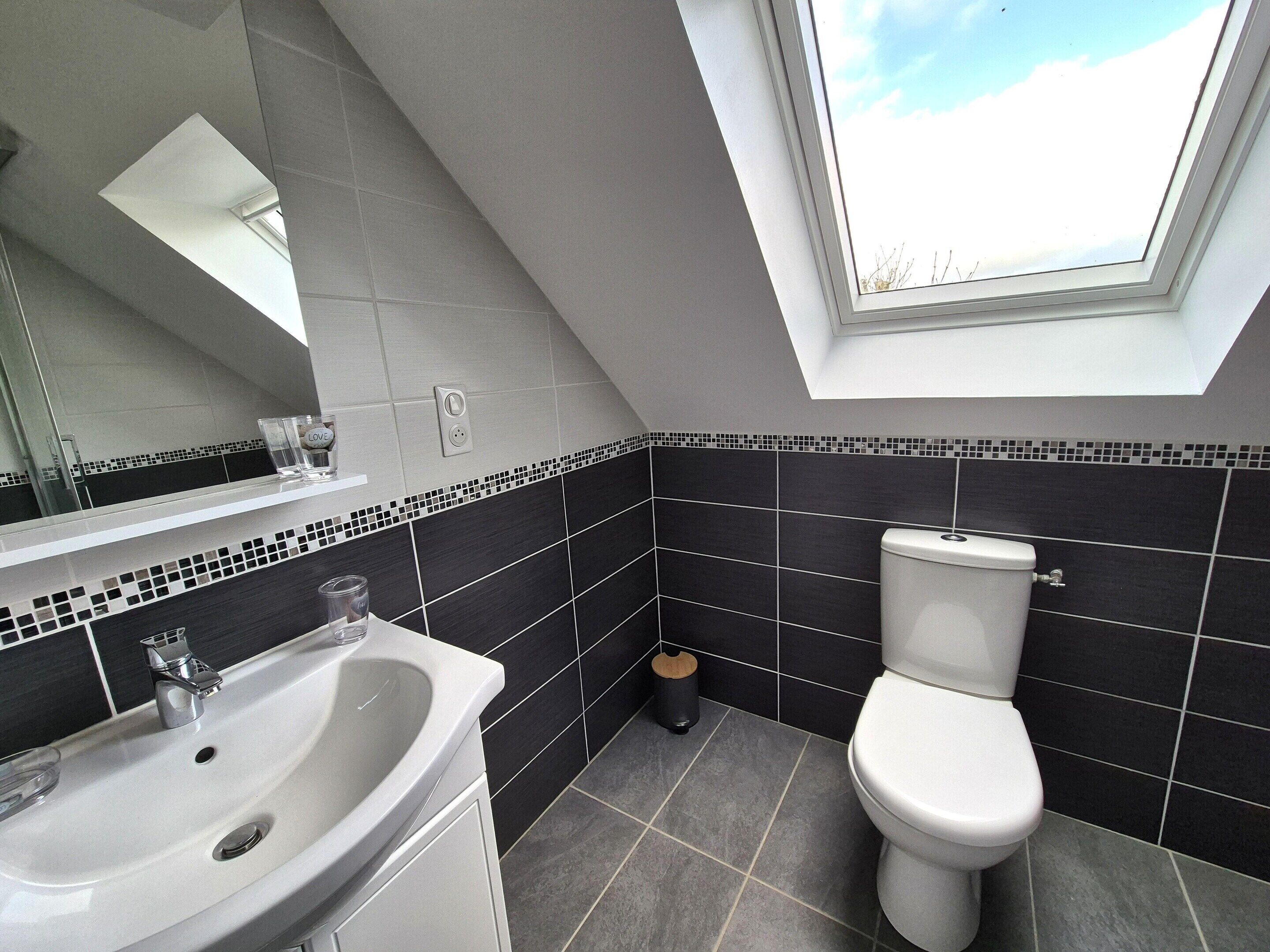 Ein modernes Badezimmer mit Oberlicht, einem weißen Waschbecken und einer Toilette.