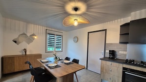 Une cuisine moderne avec un coin repas, comprenant une table en bois, des chaises noires, un four encastré et un luminaire au plafond au design original.