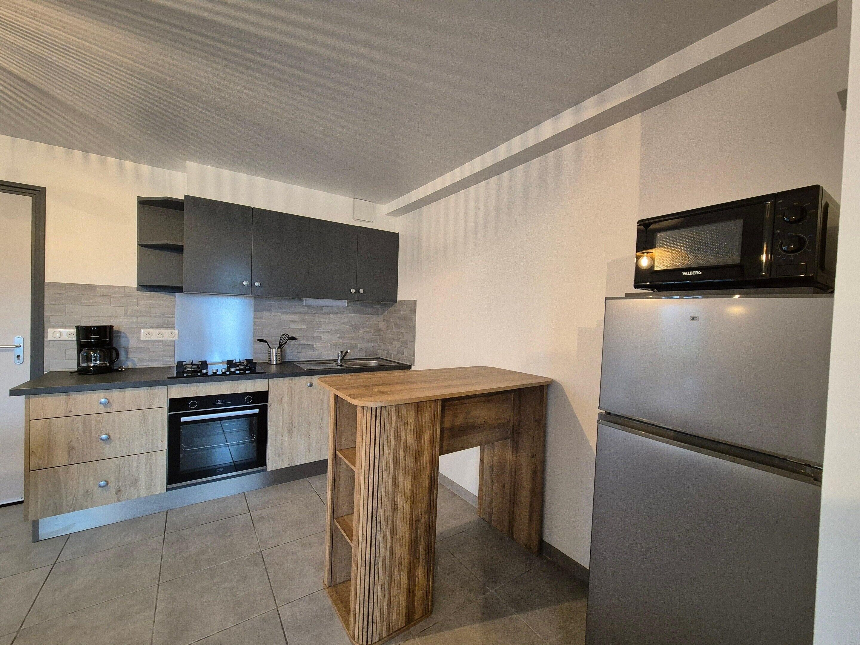 A modern kitchen with dark cabinets, a built-in microwave, a stainless steel refrigerator, a wooden table, and a dishwasher.