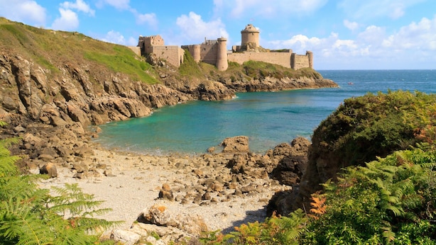 Un château côtier doté d’une structure fortifiée, un ciel d’un bleu éclatant et une côte rocheuse.