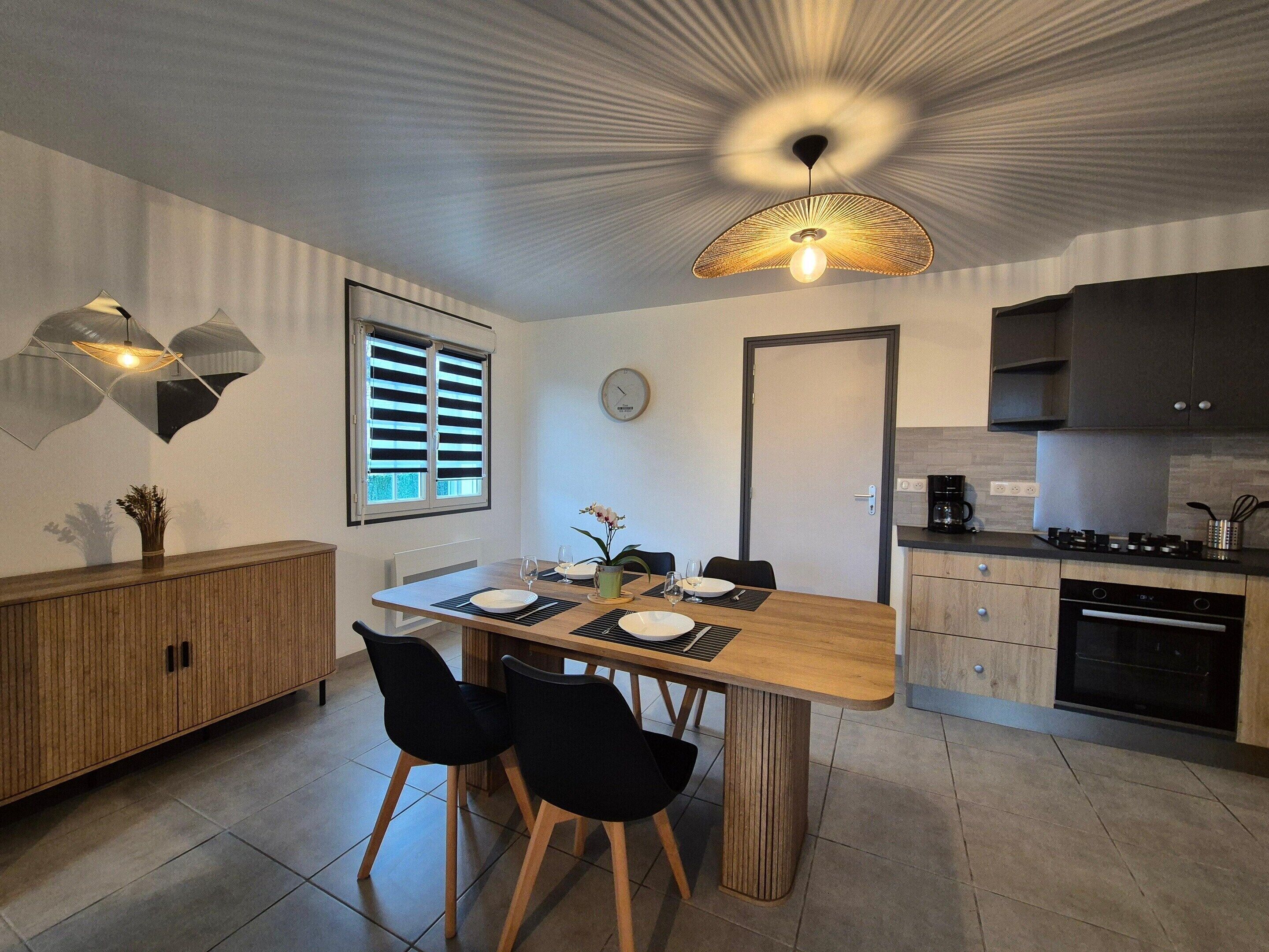 A modern kitchen with a dining area, featuring a wooden table, black chairs, and a unique ceiling light fixture.